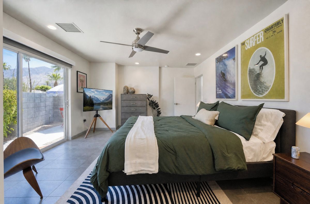A bedroom with a bed, a ceiling fan, a television, and a poster on the wall.