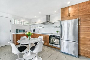 A modern kitchen with a stainless steel refrigerator, oven, and microwave. There is a dining table with white chairs and a vase with flowers. - Ocotillo Art Lounge - Historic Ocotillo Lodge (Palm Springs)