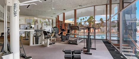 A gym with various exercise equipment, large windows, and a view of palm trees.