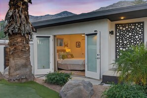 A modern house with a bedroom featuring a bed, a door with a circular pattern, and a view of the mountains. - Yellow Palms - Warm Sands (Palm Springs)