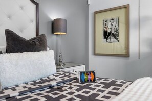 A neatly arranged bedroom with a tufted headboard, a bedside lamp, a framed picture on the wall, and a bed with patterned bedding. - Yellow Palms - Warm Sands (Palm Springs)