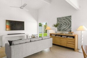 Ein modernes Wohnzimmer mit Sofa, Couchtisch, Fernseher, Bücherregal und Stehlampe.