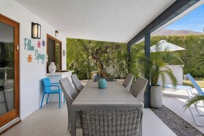 Eine überdachte Terrasse mit Esstisch, Stühlen und einem Blumentopf.