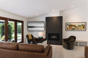 Een moderne woonkamer met een open haard, een bank, een fauteuil en kunstwerken aan de wanden.