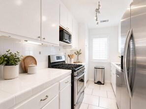 A modern kitchen with white cabinetry, stainless steel appliances, a microwave, and a trash bin. - 2BR coastal San Diego home near the pier (San Diego)