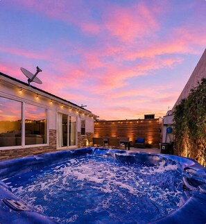 Ein Garten mit Whirlpool, Sitzgelegenheit im Freien und einem Gebäude mit Satellitenschüssel.