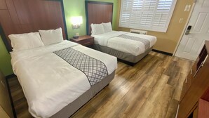 Ein Hotelzimmer mit zwei Betten, einem Nachttisch, einer Wandlampe und einem Fenster mit Jalousien.