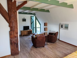 Een kamer met een houten vloer, een televisie, een houten kast, twee leren fauteuils en een radiator.