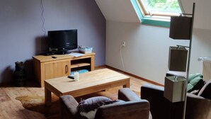 Ein gemütliches Wohnzimmer mit schrägen Wänden, einem Fernseher, einem Holztisch und einer Couch.