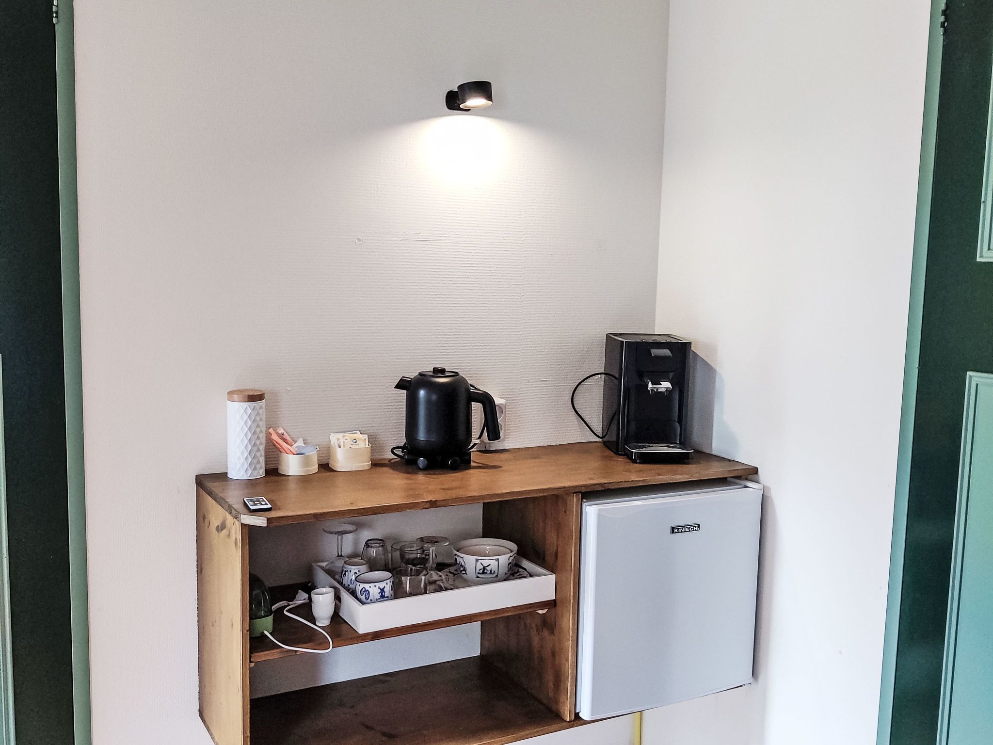 Een kitchenette met een koffiezetapparaat, waterkoker en een kleine koelkast.
