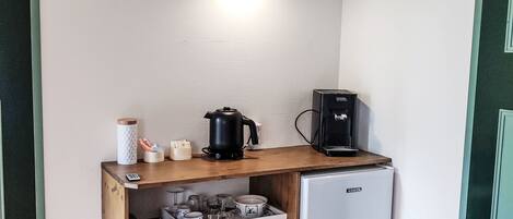 A kitchenette with a coffee maker, kettle, and a small refrigerator.