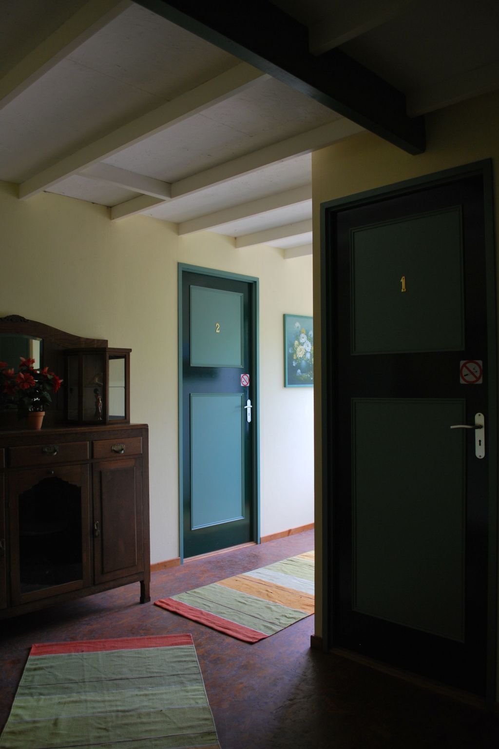 A hallway with a wooden cabinet, a green door with a number, and a mat on the floor.