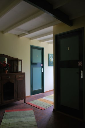 A hallway with a wooden cabinet, a green door with a number, and a mat on the floor.