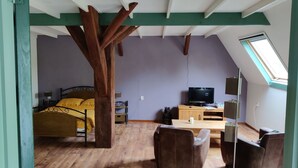 Ein Zimmer mit geneigter Decke, einem Bett, einem Fernseher, einem Schreibtisch und einem Sessel.