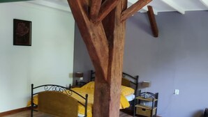 Ein Zimmer mit einer baumartigen Holzkonstruktion, einem Bett mit gelber Bettwäsche, einem braunen Ledersessel und Holzboden.