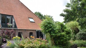 Ein Haus mit geneigtem Dach, einer Ziegel-Fassade und einem Garten mit verschiedenen Pflanzen und Blumen.