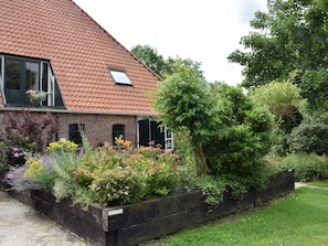 A house with a sloped roof, a brick exterior, and a garden with various plants and flowers. - Taniaburg Gästezimmer 2 by Interhome (Leeuwarden)