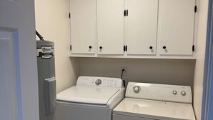 A laundry room with a front-loading washer and dryer, white cabinets above, and a door to the left.