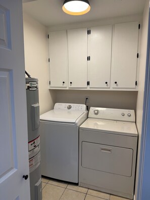 A laundry room with a front-loading washer and dryer, white cabinets above, and a door to the left.