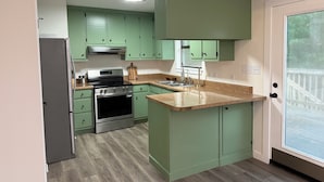 Una cocina con gabinetes verdes, un refrigerador de acero inoxidable, horno empotrado y encimera de granito.