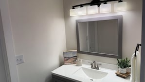 Un baño con un lavamanos blanco, un espejo grande y una lámpara de pared.