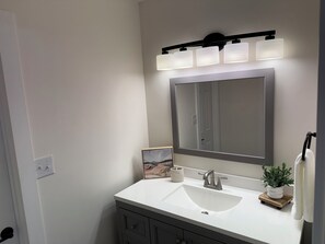 Une salle de bain avec un lavabo blanc, un grand miroir et un luminaire fixé au mur.