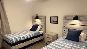 Un dormitorio con dos camas, cada una con cubrecama a rayas, una mesita de noche, un cajón y una lámpara de pared.