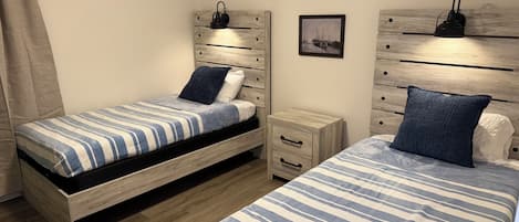 Une chambre à coucher avec deux lits, chacun recouvert d’une couvre-lit à rayures, une table de chevet, un tiroir et une lampe fixée au mur.