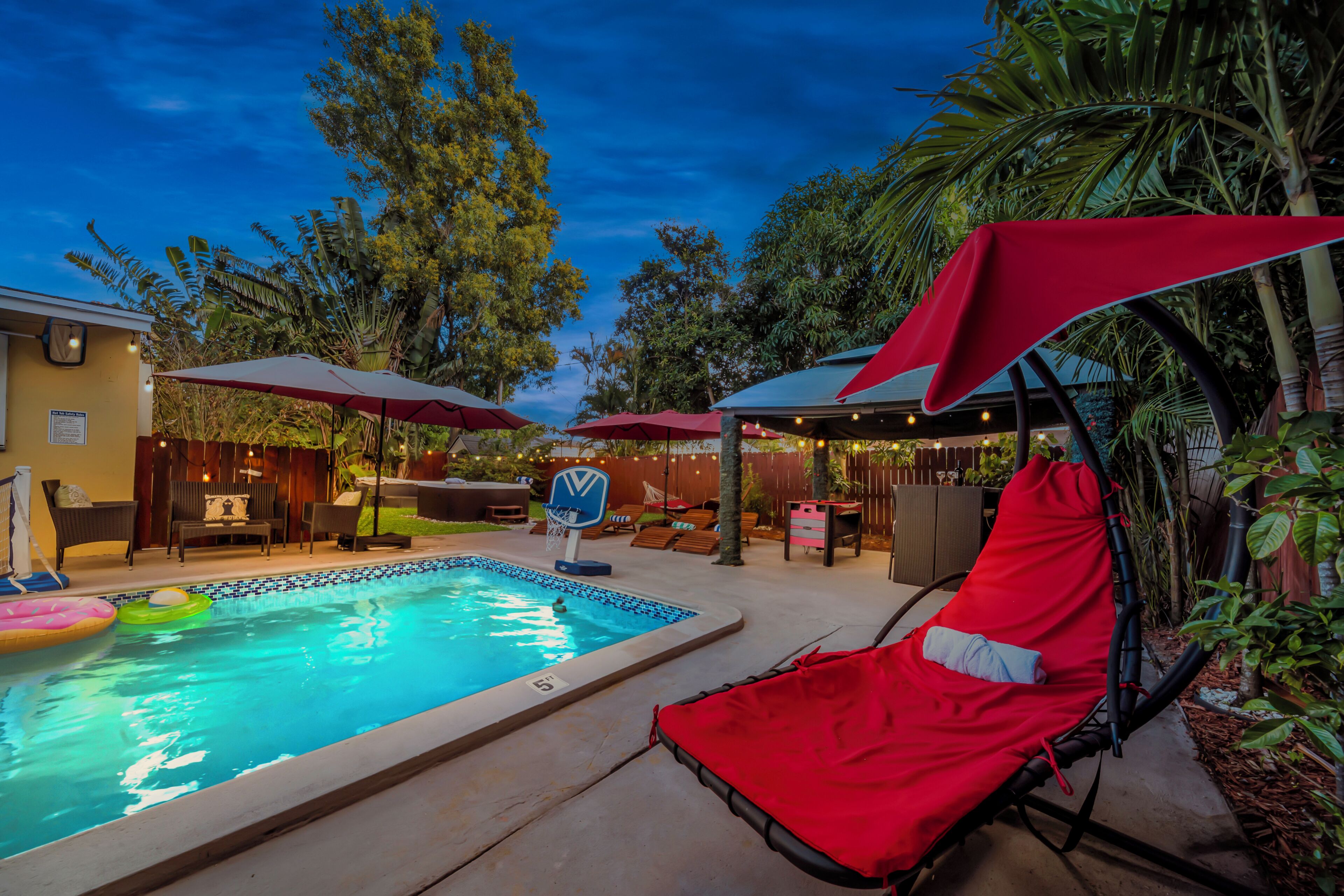 Une piscine entourée d’arbres et d’une clôture en bois, avec des chaises longues et des parasols à proximité.