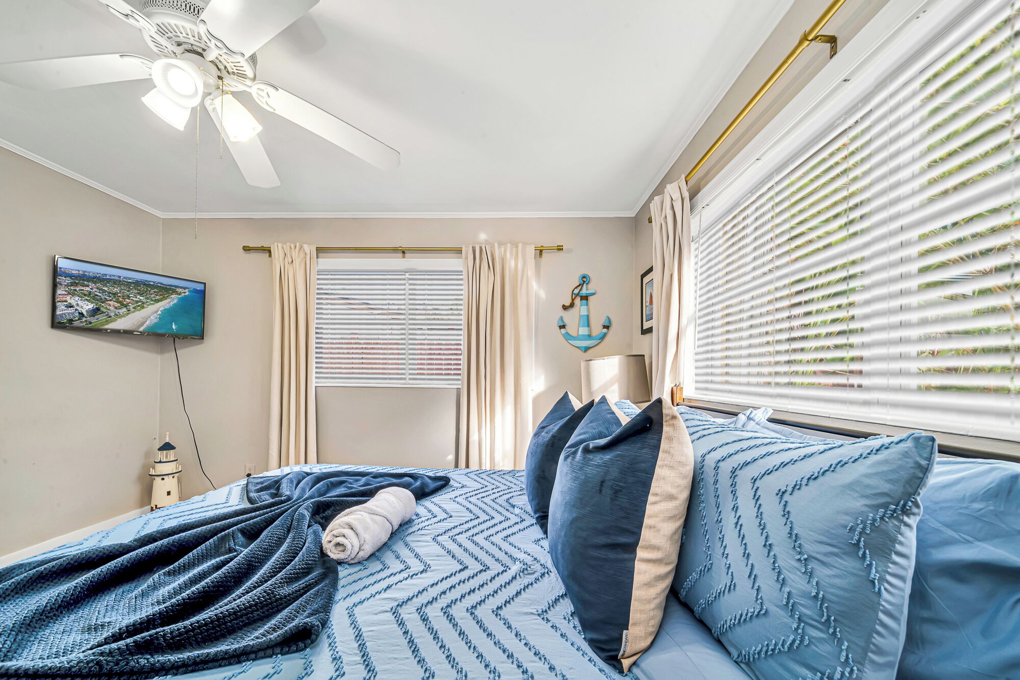 A bedroom with a bed, a ceiling fan, a TV, and a window with blinds.