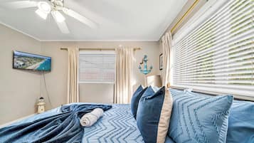 A bedroom with a bed, a ceiling fan, a TV, and a window with blinds.