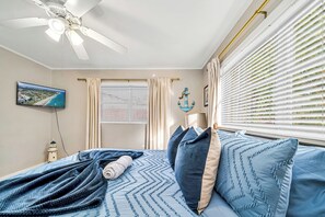 Ein Schlafzimmer mit Bett, Deckenventilator, Fernseher und einem Fenster mit Jalousien.