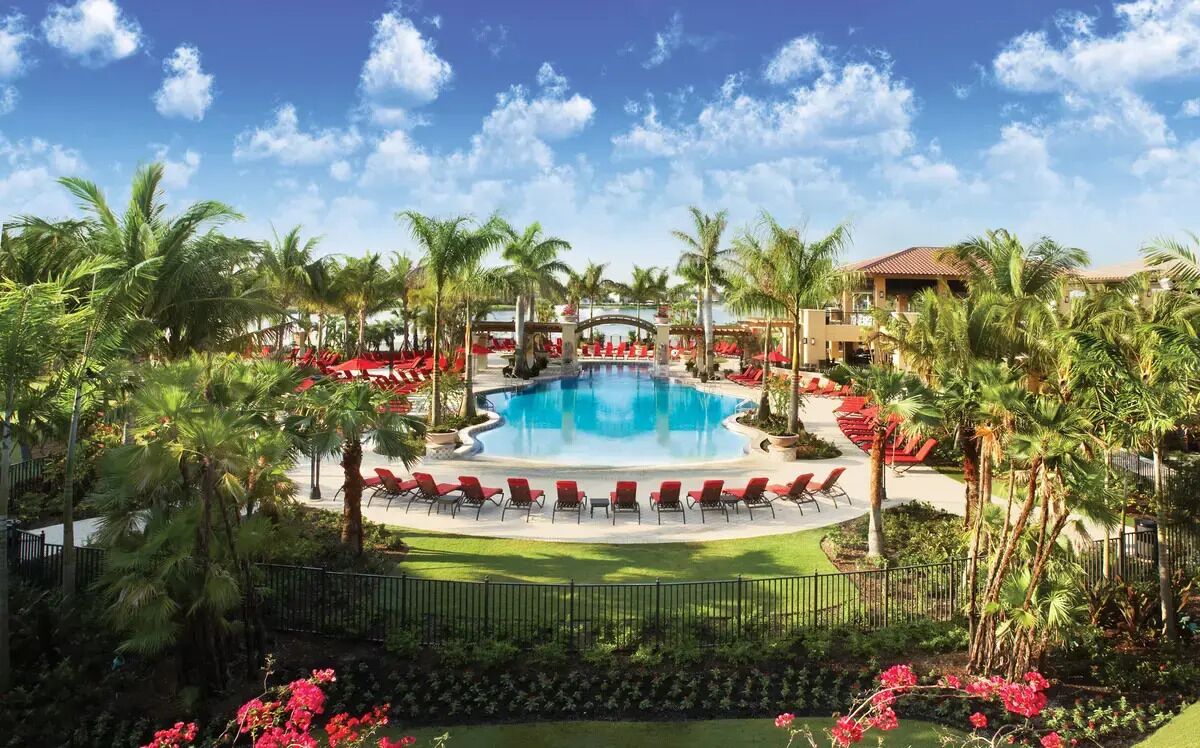 Ein Poolbereich eines Resorts mit Palmen, roten Liegestühlen und wolkenlosem, blauem Himmel.
