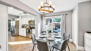 Una cocina moderna con electrodomésticos de acero inoxidable, un comedor con mesa y sillas de vidrio, y vistas al exterior.