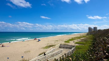 A beach with a wooden boardwalk leading to the shore, clear blue sky, and distant buildings.