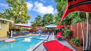 Una piscina con trampolín, rodeada de sombrillas rojas y sillas de descanso.
