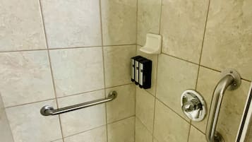 A shower stall with a handrail, a handheld showerhead, and a soap dispenser.