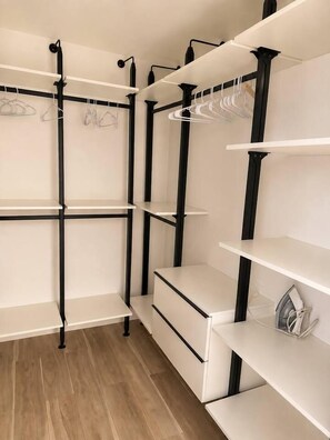A closet with multiple shelves and hanging space, featuring a minimalist design with black metal supports and white shelves. - Woodland Hills Hidden Waterfall Oasis | Pool & BBQ (Los Angeles)