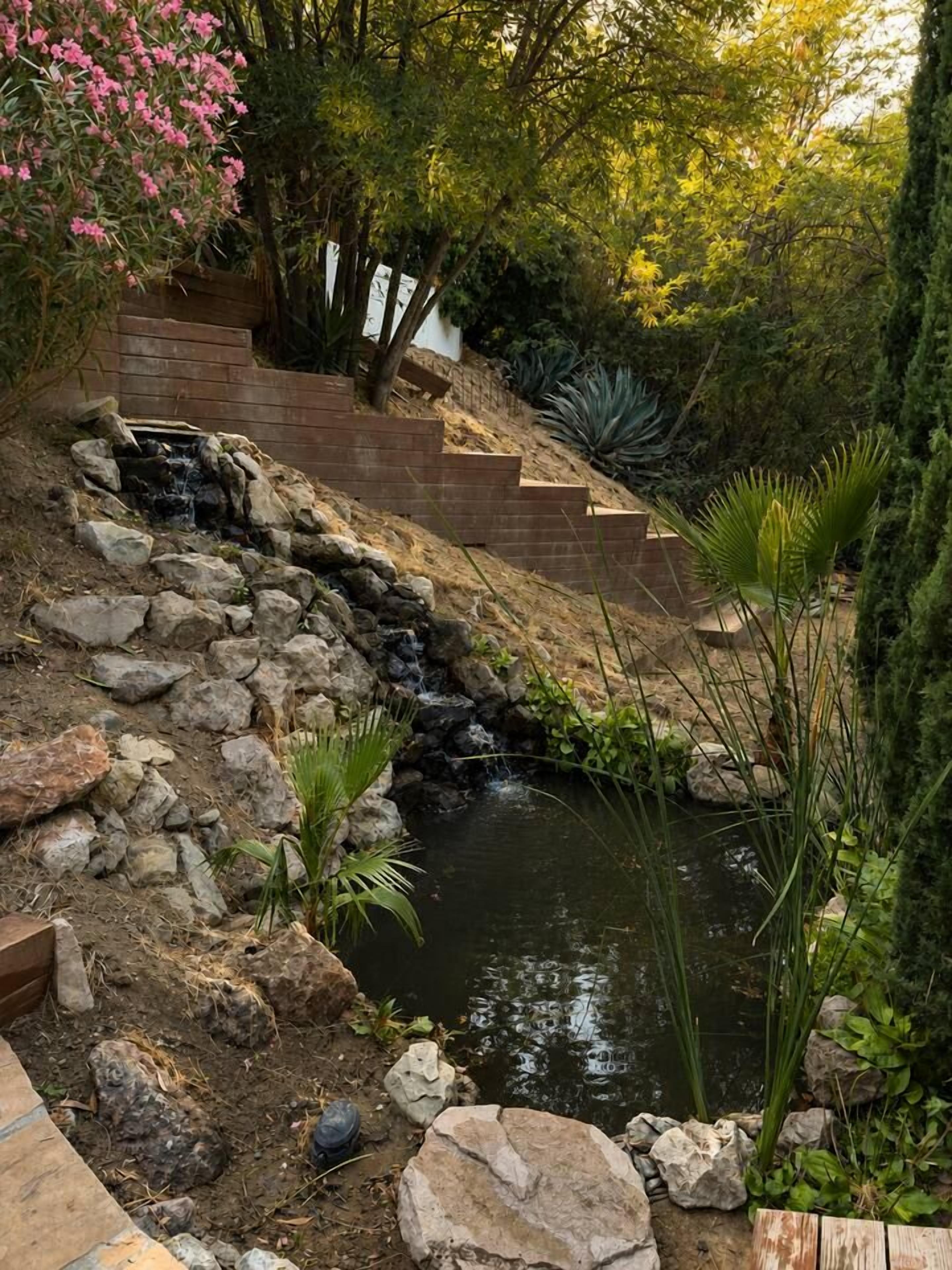 A garden with a small waterfall, a wooden staircase, and various plants.