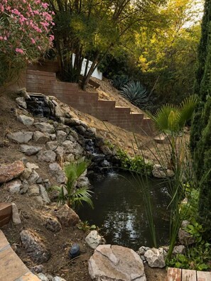 Een tuin met een kleine waterval, een houten trap en diverse planten.