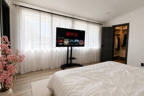 A bedroom with a bed, a TV displaying Netflix content, a window with sheer curtains, and a closet. - Woodland Hills Hidden Waterfall Oasis | Pool & BBQ (Los Angeles)