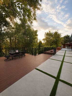 Een terras buiten met een tafel en stoelen, omgeven door een zwart metalen hek, en een betonnen gebied met graspatronen.