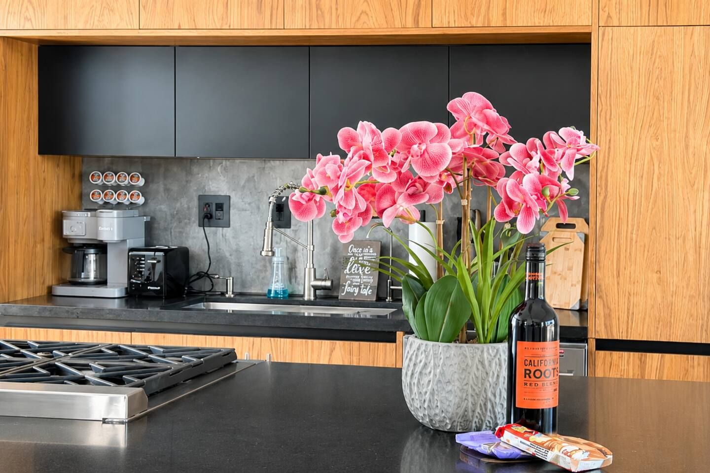 Une cuisine moderne équipée d’une cuisinière intégrée, d’une machine à café et d’une orchidée en pot.