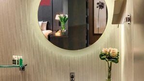 A bathroom with a round mirror, a white sink, a vase with flowers, and a towel rack. - Dominion Grand Suites Toronto (Toronto)