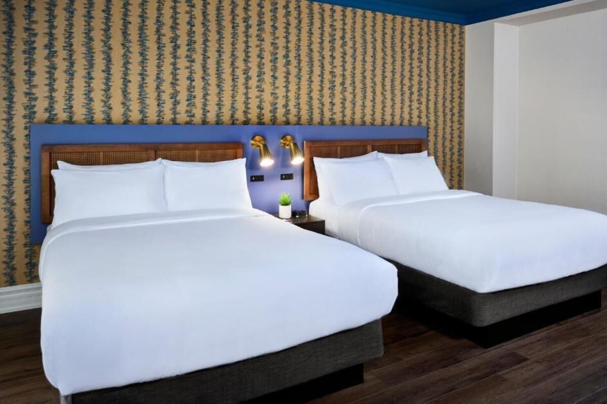 Een hotelkamer met twee bedden, behang met een patroon en een houten hoofdbord.