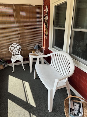 A room with a white plastic chair, a small round table, and a wicker basket containing a magazine.