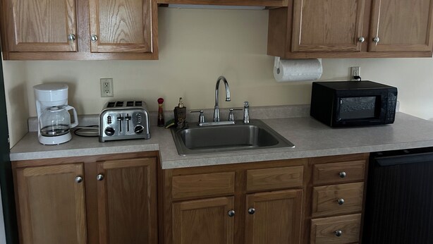 A kitchen with wooden cabinets, a stainless steel sink, a coffee maker, a toaster, and a microwave.