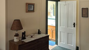 A room with a wooden dresser, a lamp, a framed picture, and a door leading to a kitchen.