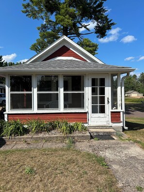 A small, single-story house with a red and white exterior, a front porch, and a large window. - Cozy 1-bedroom cabin in fabulous Minocqua with AC (Minocqua)