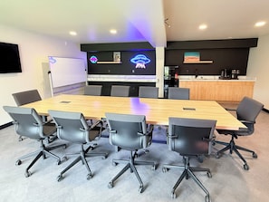 Un salón de conferencias con una gran mesa de madera, seis sillas de oficina negras, una pizarra y un letrero de neón.